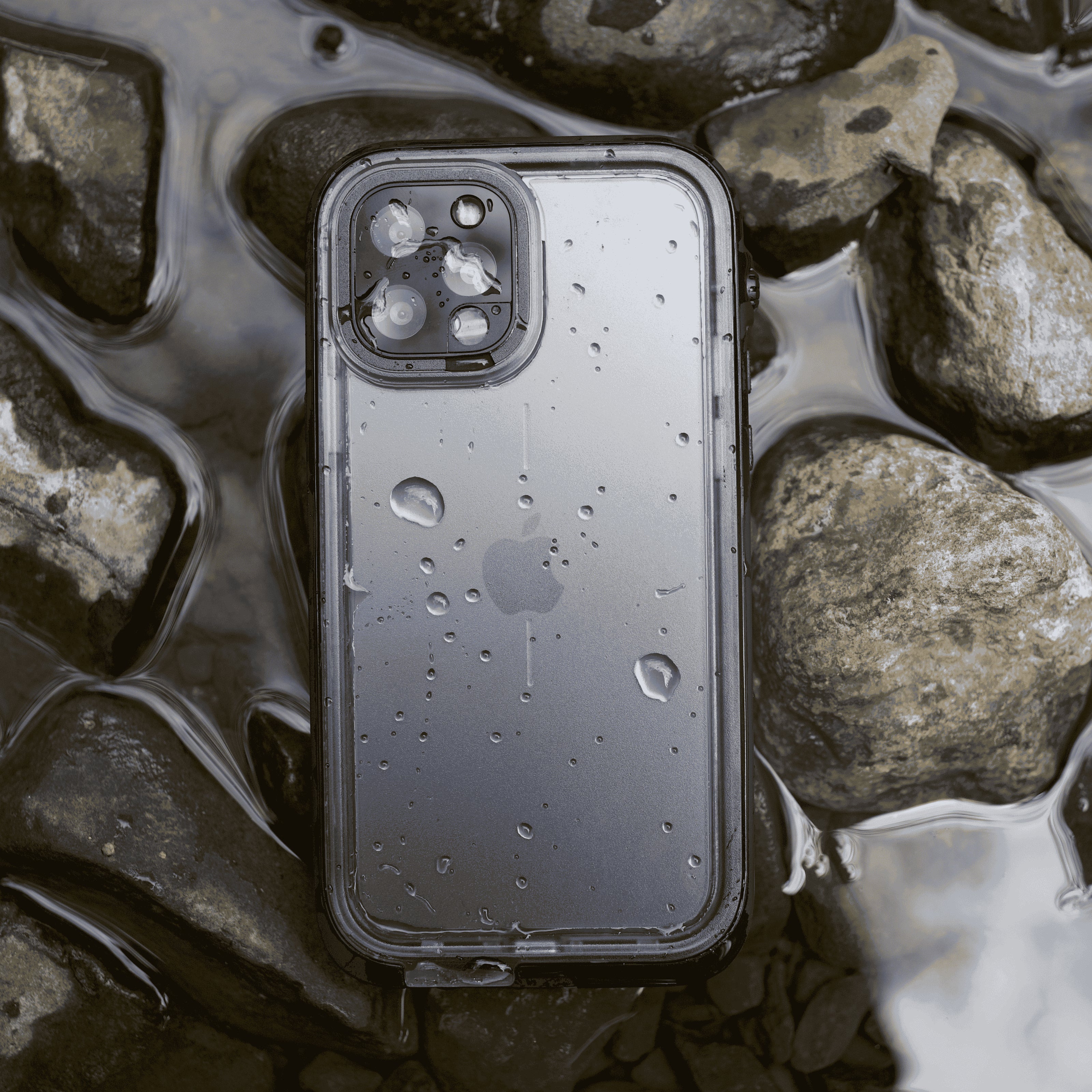 Catalyst waterproof Case laying on brown rocks on a water stream with water reflecting the sky
