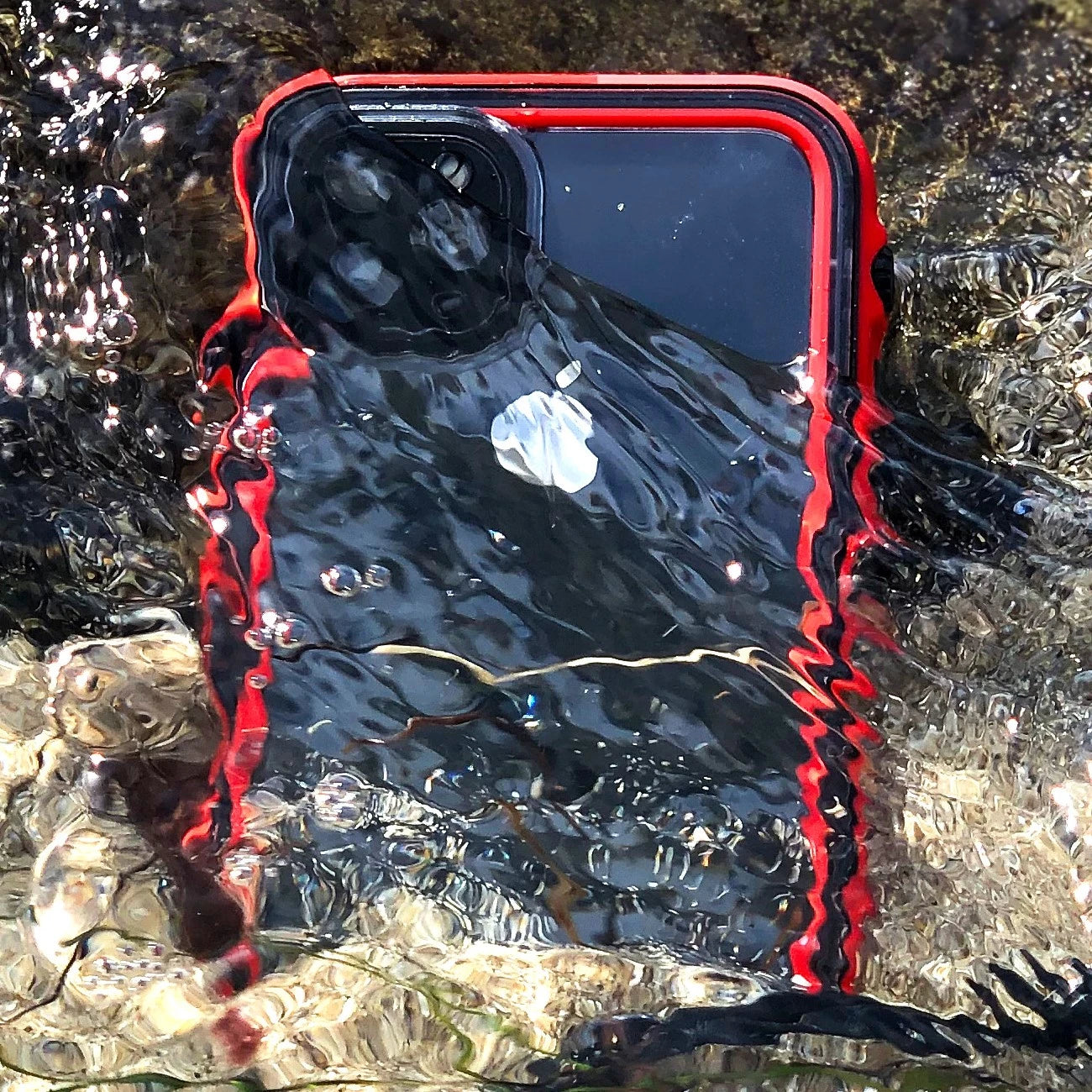 A red Catalyst iPhone Waterproof Case, Total Protection, expertly designed against water and dirt, submerges with its logo and cameras visible amid ripples and bubbles.