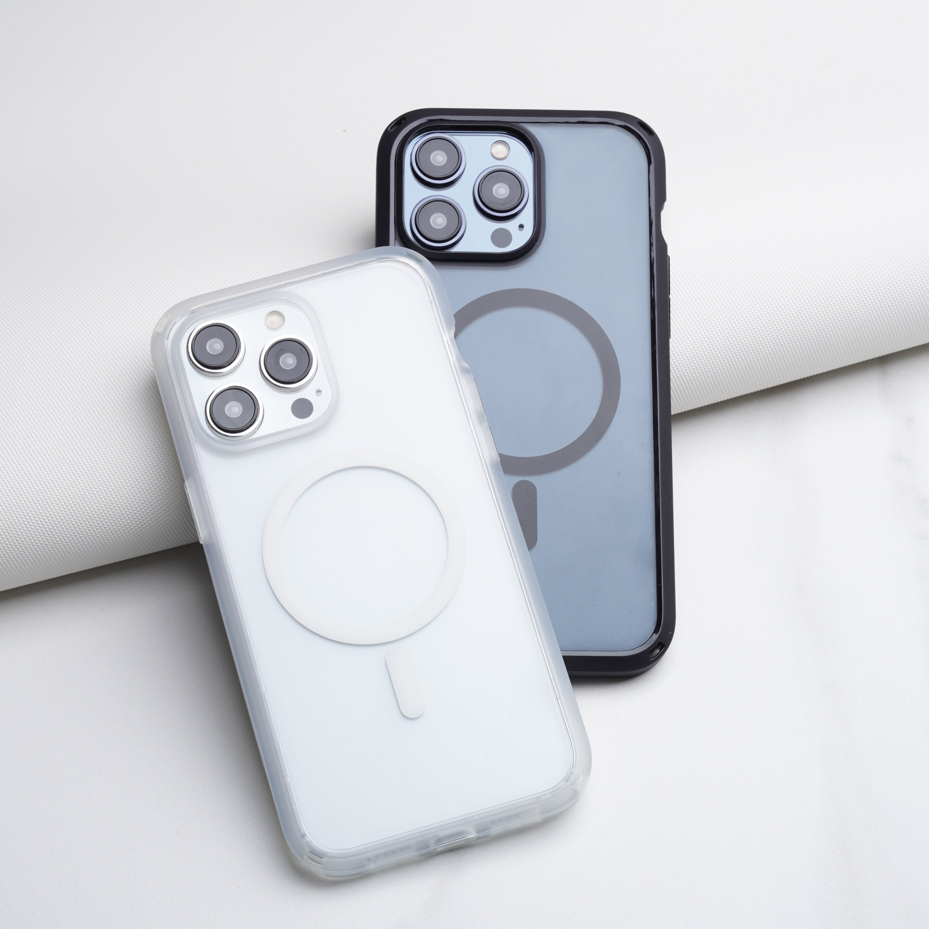 Two sleek smartphones in Catalyst drop proof cases, magsafe compatible, one white and translucent, the other black and opaque, are displayed against a minimalistic white background.