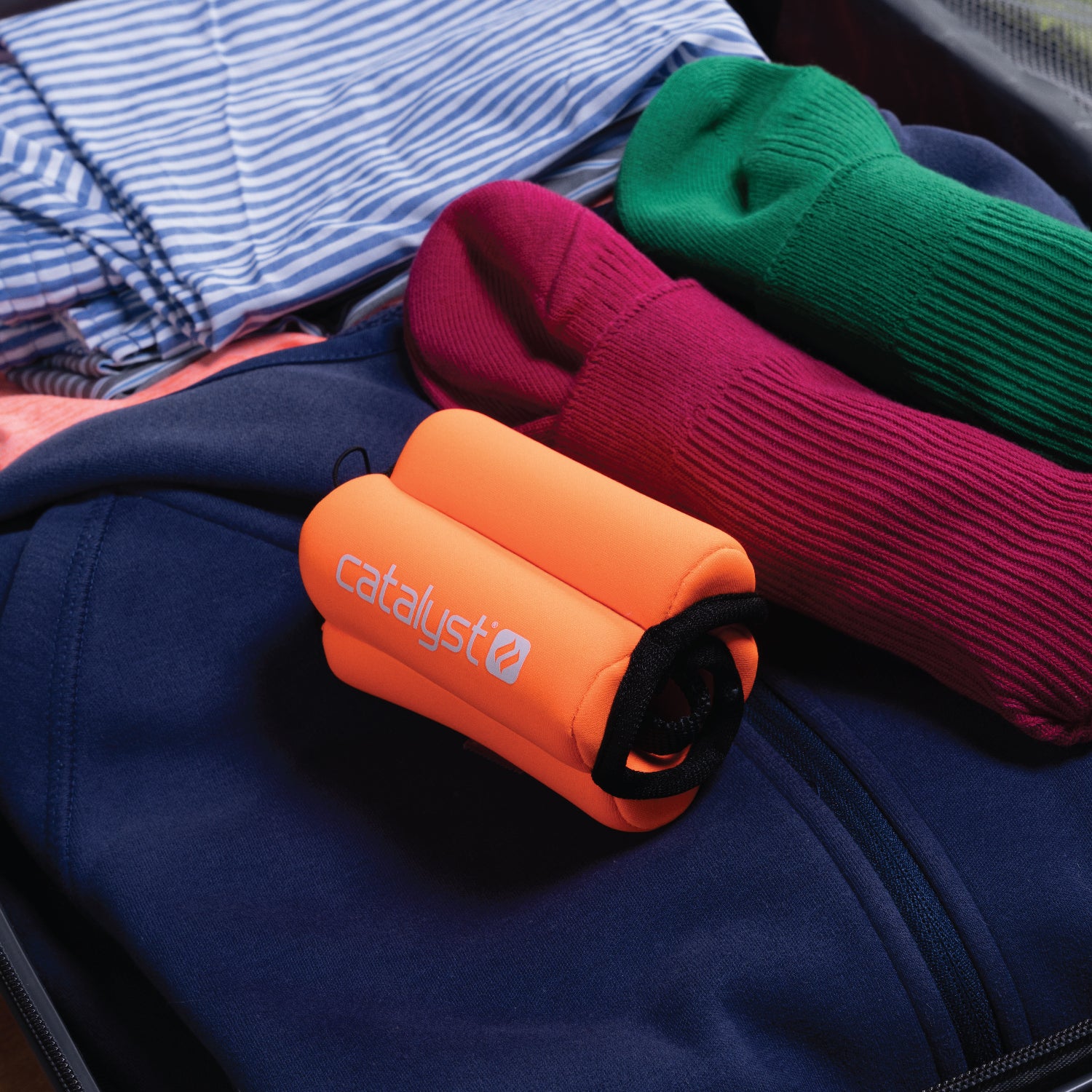 Catalyst orange floating wrist lanyard showing next to clothings inside luggage